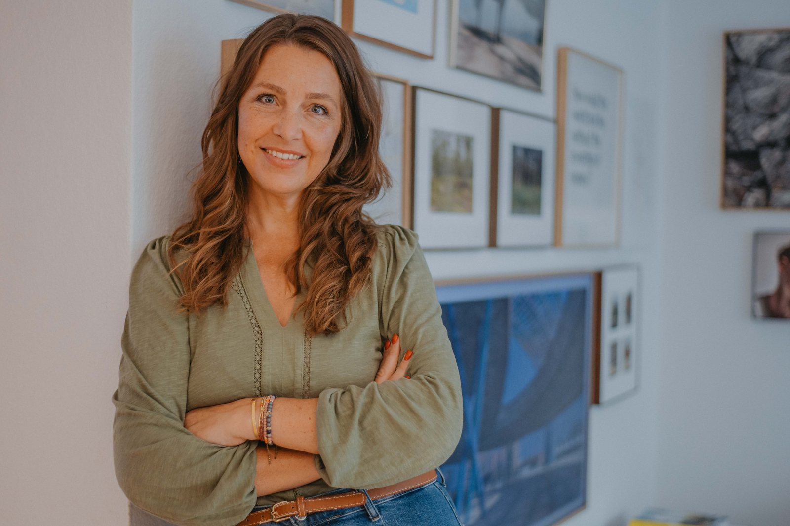 Diana Thomas lehnt lächelnd an einer Wand mit Bildern, Coaching in Celle